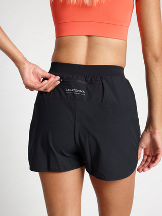 Woman wearing black athletic shorts with zip back pocket with a minimalistic TAGATONNA Athletic Design Lab  logo on a light gray background