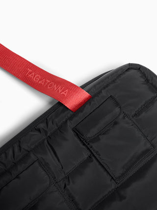 Black puffer bag with coral handles and 'TAGATONNA'  reflective branding on a white background