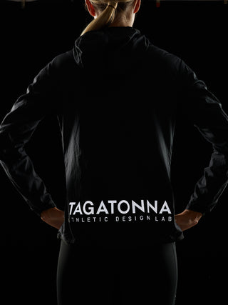 Woman wearing  black jacket  and black shorts with reflective TAGATONNA Athletic Design Lab logo on the lower back